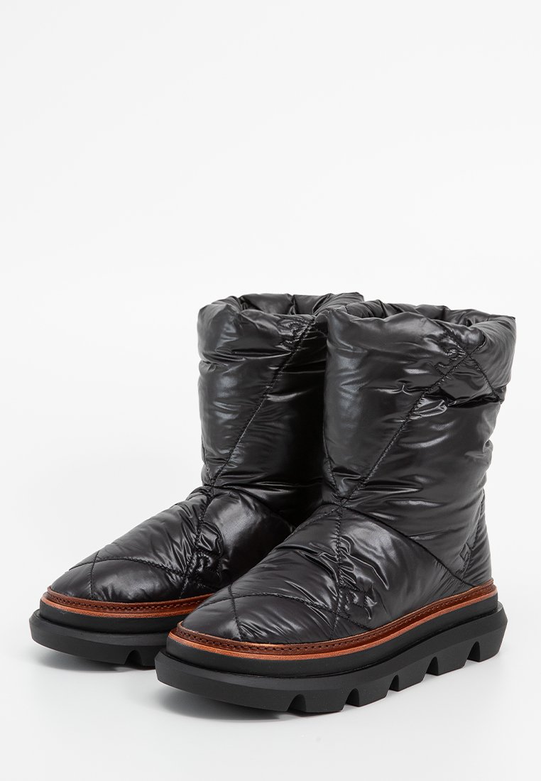 Botas acolchadas negras con un acabado brillante, que cuentan con una suela de goma gruesa y una mediasuela marrón en contraste. Collar acolchado con textura fruncida.