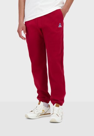 Red sweatpants made of soft fabric, featuring an elastic waistband and cuffs. A small logo is displayed on the left thigh.