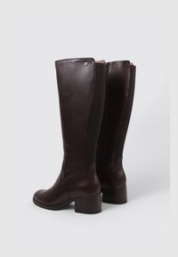 Brown leather knee-high boots with a block heel, featuring elastic side panels and a zip closure at the back. Minimalist design, no visible patterns.