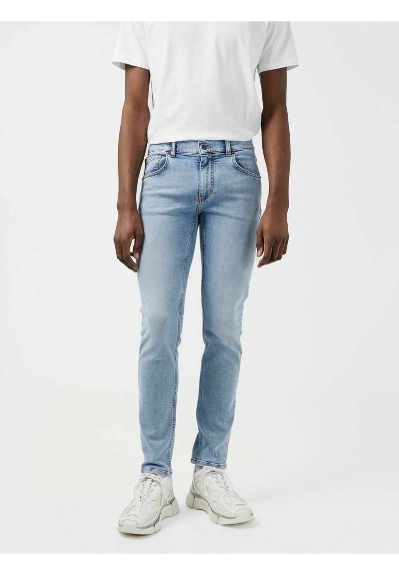Lichtblauwe denim jeans met een slim fit. Bevat vijf zakken, een knoop- en ritssluiting, en subtiele vervaging. Gepaard met witte sneakers.