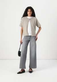 Beige kortermet cardigan over en hvit skjorte, kombinert med vide grå jeans. Svarte leiligheter med prikkete mønster og en liten svart crossover-veske.