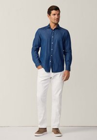 Camicia in denim blu scuro con bottoni, pantaloni bianchi e sneakers casual marroni. La camicia ha un colletto classico e maniche lunghe.