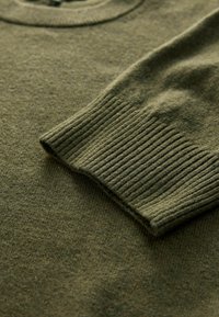 Olivově zelený pletený svetr s kulatým výstřihem, žebrovanými manžetami a hladkým povrchem. Tkanina vypadá měkce a mírně vlněně s jednotným vzorem.