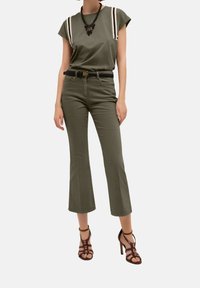 Olivově zelené tričko se smetanovými pruhy, světle olivové kalhoty s vysokým pasem a hnědé podpatky, doplněné černým opaskem a náhrdelníkem z perliček.