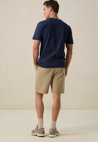 Navyblauwe katoenen t-shirt, beige shorts, grijze sneakers en lichtgekleurde sokken. Casual pasvorm met korte mouwen en een eenvoudig ontwerp.
