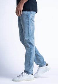 Lichtblauwe denim jeans met een rechte pijp, met een vervaagd textuur en een standaard vijf-pocket layout, gedragen met witte sneakers.