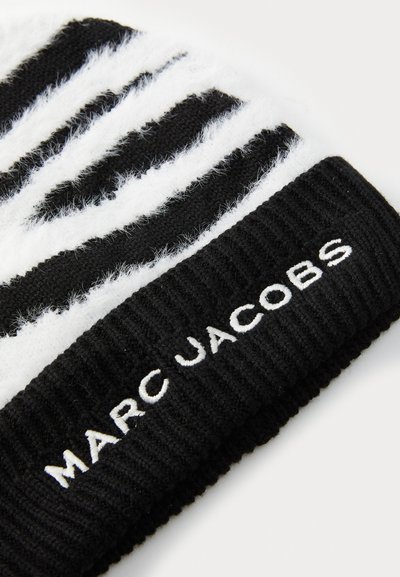 Svart och vit randig stickad mössa med fluffig textur. Har en djärv "MARC JACOBS"-logotyp i vitt på en svart ribbad kant.