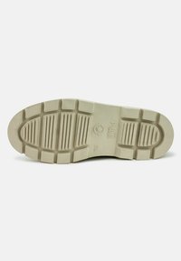 Suela de zapato de goma con un patrón de relieve texturizado, que presenta ranuras grandes y pequeñas para mejorar el agarre. Color beige claro, con marca en relieve.