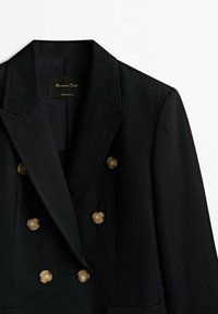 Blazer noir croisé en tissu lisse, doté de boutons dorés, de revers crantés et de détails de couture minimalistes.