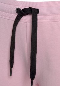 Lichtroze sweatpants met een zwarte trekkoord. De tailleband heeft een geribbelde textuur met een knoopdetail in het midden.