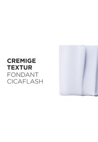 Kremowa biała tekstura balsamu rozłożona na białym tle z czarnym napisem „Cremige Textur Fondant Cicaflash”.