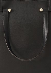 Borsa a mano in pelle nera con una consistenza liscia, due manici corti e accentuazioni di perle ben visibili sugli attacchi.