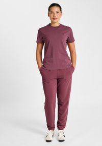 Bordowy komplet odzieży sportowej składający się z t-shirtu z okrągłym dekoltem oraz spodni dresowych z elastycznymi mankietami. Tkanina wydaje się miękka, z minimalistycznym designem.
