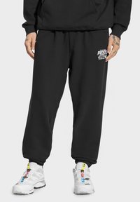 Czarne dresy z elastyczną talią, ściągaczami na kostkach i białym logo po lewej stronie. Wykonane z miękkiego, teksturowanego materiału.