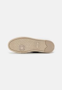 Suela de zapato con un material de goma texturizado y un patrón de zigzag en beige, marcado con "TOMS" y un acento circular en el centro.