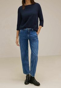 Námořnická modrá halenka s dlouhým rukávem, kombinovaná s rovnými modrými džíny a černými kotníkov�ými botami. Jednoduchý design s hladkou texturou a přiléhavým střihem.