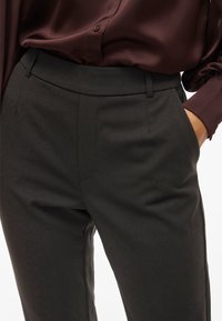 Prilagojeni temno sivi hlače z gladko teksturo tkanine, opremljene z stranskimi žepi in ravnim sprednjim dizajnom. Slogane z globoko burgundno bluzo.