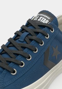 Blue canvas sneaker with gray laces, silver eyelets, and a prominent black and white All Star logo on the tongue. Features a star emblem.