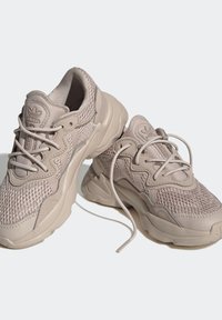 Beiga sportskor med ett nätövre, texturerade detaljer, gummisula och kontrasterande snören. Designade för andningsförmåga och komfort.