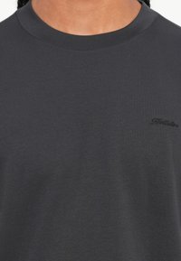 Κοντινό πλάνο του λαιμού ενός σκούρου γκρι μπλουζάκι με διακριτό κεντημένο λογότυπο "Hollister" στο επάνω αριστερό μέρος του στήθους.