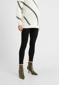 Suéter de punto beige con rayas diagonales negras, combinado con leggings negros y botas de tobillo de patrón de cocodrilo en verde olivo con puntera afilada.