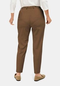 Brown tailored trousers with a high waist, slim fit, and crease details. Paired with beige slip-on shoes, viewed from the back.