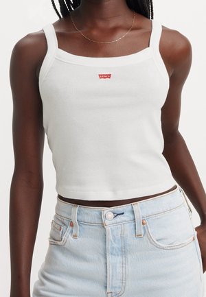 Biały prążkowany top na ramiączkach z kwadratowym dekoltem i cienkimi szelkami. Na środku małe czerwone logo Levi's. Połączony z jasnoniebieskimi, wysokim stanem dżinsami.
