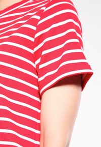 T-shirt à manches courtes rayé horizontalement rouge et blanc porté sur le haut du bras et l'épaule d'une personne sur un fond clair.