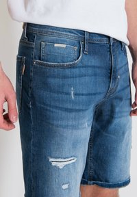 Shorts in denim blu medio, con un design strappato e orlo sfrangiato e una leggera sfumatura. Include tasche e dettagli con etichetta del marchio.