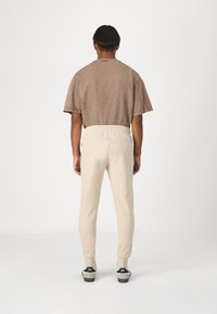 Beige Sweatpants mit elastischem Bund, verjüngten Beinen und Bündchen. Kombiniert mit einem braunen, leicht übergroßen T-Shirt. Minimalistisches Design.