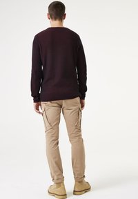 Suéter de punto a rayas navy y burdeos, combinado con pantalones cargo beige. Botas de color tostado con superficie texturizada. Diseño simple, sin logotipos visibles.