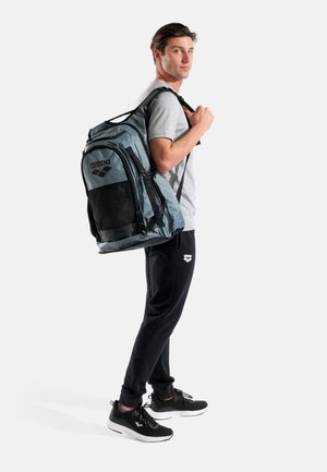 Mochila deportiva gris con panel de malla, detalles en negro y múltiples compartimentos. Correas acolchadas ajustables y material resistente.