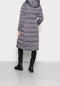 Abrigo acolchado gris con diseño de cuadros horizontales, capucha y mangas largas, combinado con botas negras hasta el tobillo y leggings.