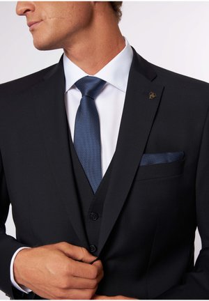 Schwarze Sakkjacke mit einem weißen Hemd und einer marineblauen Krawatte mit Punkten. Enthält ein Einstecktuch im passenden Muster und eine dekorative Reversnadel.