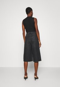 Musta ribbineulottu hihaton toppi, yhdistettynä korkeavyötäröisiin, leveälahkeisiin tummansinisiin denimheisiin culottes-housuihin. Asu on minimalistinen ja siinä on jäsennelty siluetti.