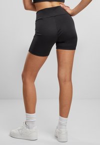 Fekete, magas derekú, sima felületű, rugalmas anyagból készült shorts, fehér sportcipővel és bokáig érő, bordás zoknikkal párosítva.