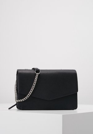 Sac bandoulière en cuir noir texturé avec bandoulière chaîne argentée, forme rectangulaire, et fermeture à rabat de style enveloppe sur une surface blanche.