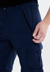 Mörkblå cargo-byxor med elastisk midja, med en dragkedjeficka och en sidoficka med klaff, tillverkade av mjukt tyg.