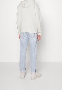 Felpa grigia chiara con cappuccio e cordino, abbinata a jeans azzurri con risvolto. L'outfit è completato da sneaker beige.