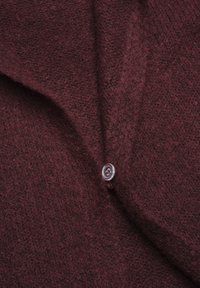 Bordeaux ullkofta med en strukturerad stickning, v-ringad design och en klar plastknapp vid kragen för stängning.