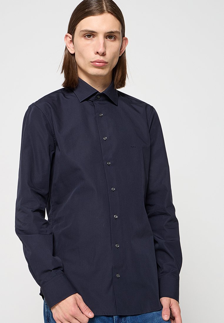 Camicia blu navy con colletto strutturato, maniche lunghe e branding discreto sul petto. Tessuto liscio con una vestibilità classica.