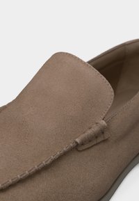 Καφέ μοκασίνι από σουέτ με λεπτομερείς ραφές κατά μήκος του επάνω άκρου και λείο ταμπά εσωτερικό επένδυση.