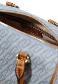 Blauwe handtas met patroon en accenten van lichtbruin leer, voorzien van een ritssluiting en een binnenvak. De gestructureerde oppervlakte verhoogt de visuele aantrekkingskracht.