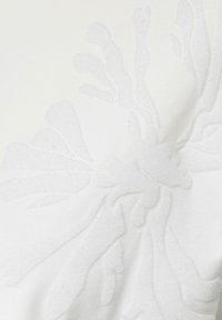 White fabric featuring a textured floral pattern in a slightly darker shade, giving a subtle contrast and an embossed appearance.