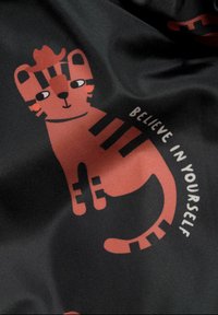 Tecknad kattdesign i orange-röd på svart bakgrund, med ränder och texten "TRO PÅ DIG SJÄLV" i vitt. Slät textur.