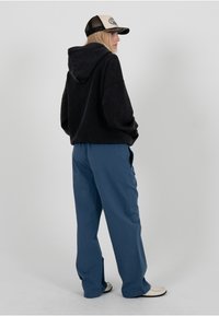 Sweat-shirt à capuche noir avec une coupe décontractée, associé à un pantalon bleu ample. La tenue a un aspect casual et texturé avec des détails minimaux.