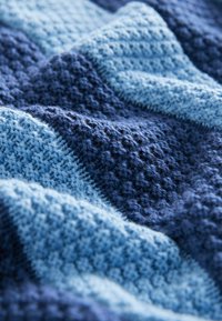 Strickdecke mit unterschiedlichen Blautönen in einem Wellenmuster, gefertigt aus einem weichen, flauschigen Garn. Glatte und gemütliche Textur.