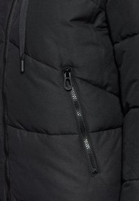 Veste matelassée noire avec une poche zippée sur le côté gauche, motif de couture horizontale et texture extérieure lisse.