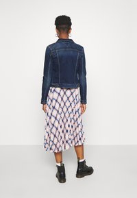 Mörkblå denimjacka med en figursydd design, bärs över en mönstrad plisserad kjol med rosa och blå nyanser. Svarta ankelboots ingår.