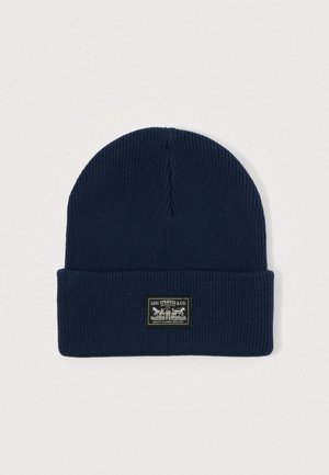 Dark blue knit beanie with a folded cuff. Features a rectangular black label with white text and a graphic of horses.